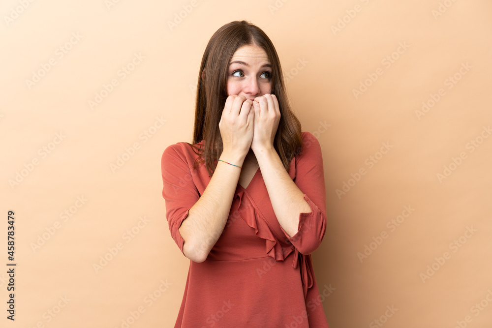 Young caucasian woman isolated on beige background nervous and scared putting hands to mouth Young caucasian woman isolated on beige background nervous and scared putting hands to mouth