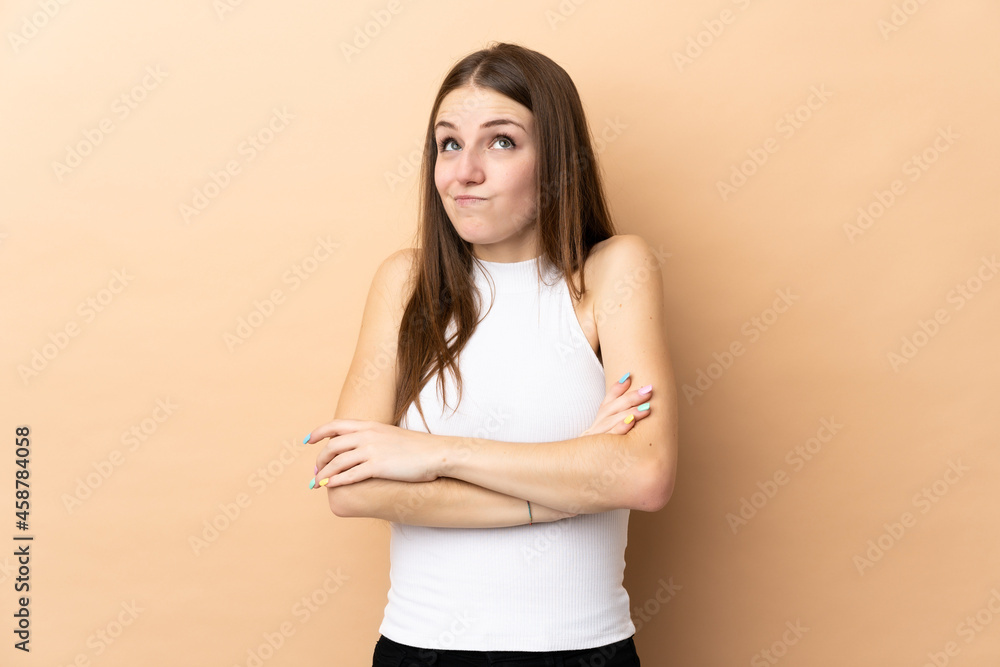 Young caucasian woman isolated on beige background making doubts gesture while lifting the shoulders Young caucasian woman isolated on beige background making doubts gesture while lifting the shoulders