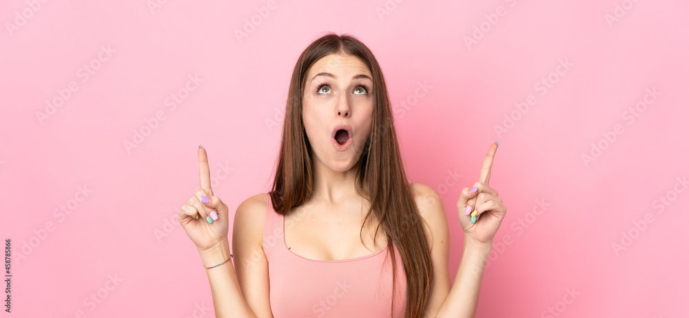 Young caucasian woman isolated on pink background surprised and pointing up
