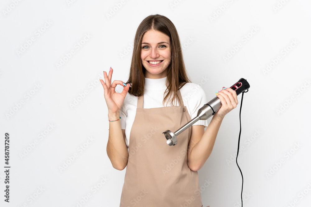 Young woman using hand blender isolated on white background showing an ok sign with fingers Young woman using hand blender isolated on white background showing an ok sign with fingers