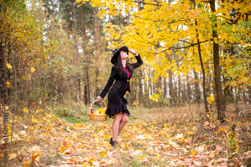 Cheerful smiling young woman surrounded by alling yellow leaves celebrate Halloween in witch costume