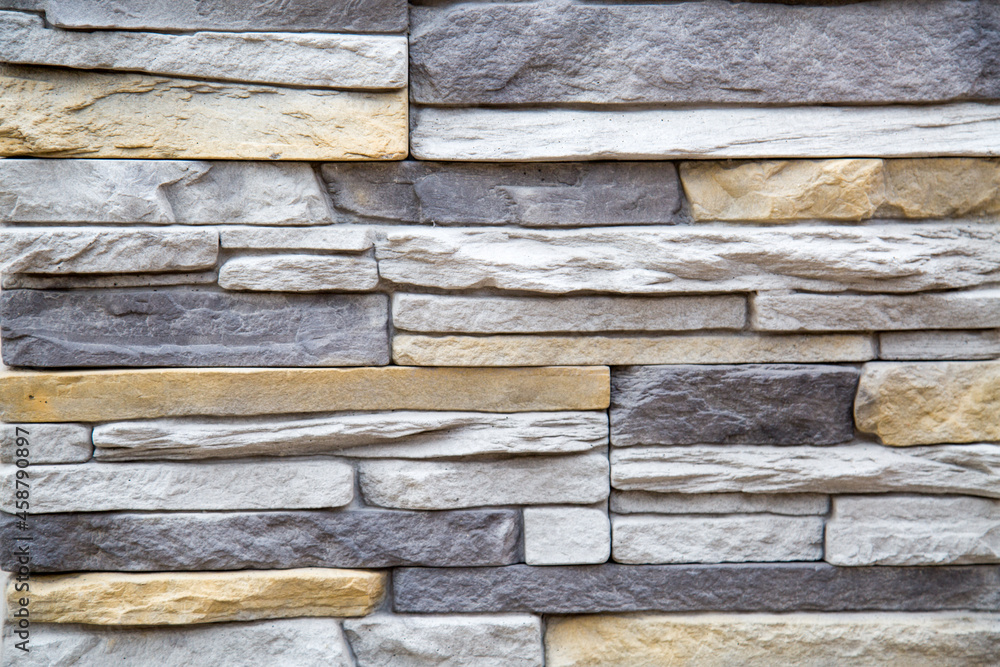 The background of the wall is made of artificial stone of an elongated irregular shape in gray and white. Backgrounds texture design. The background of the wall is made of artificial stone of an elongated irregular shape in gray and white. Backgrounds texture design.