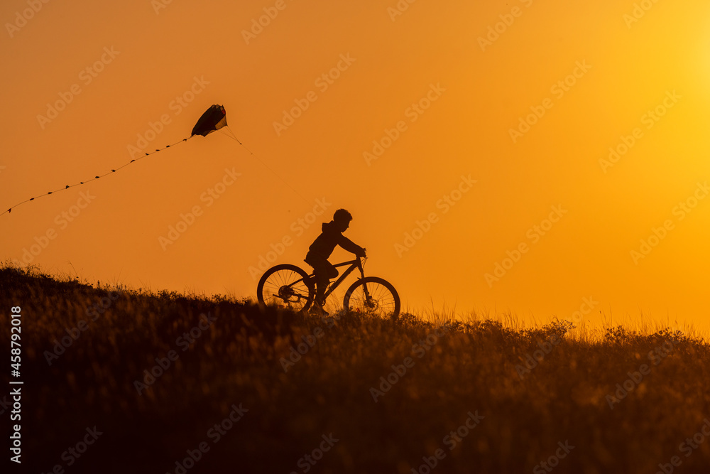 Obraz premium Silhouette of a child riding a bicycle with a kite in his hand
