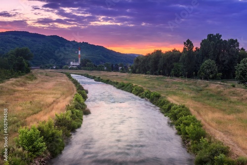 Panoramic view of blurred motion Nisava river in Pirot and distant old factory during vivid, colorful sunset