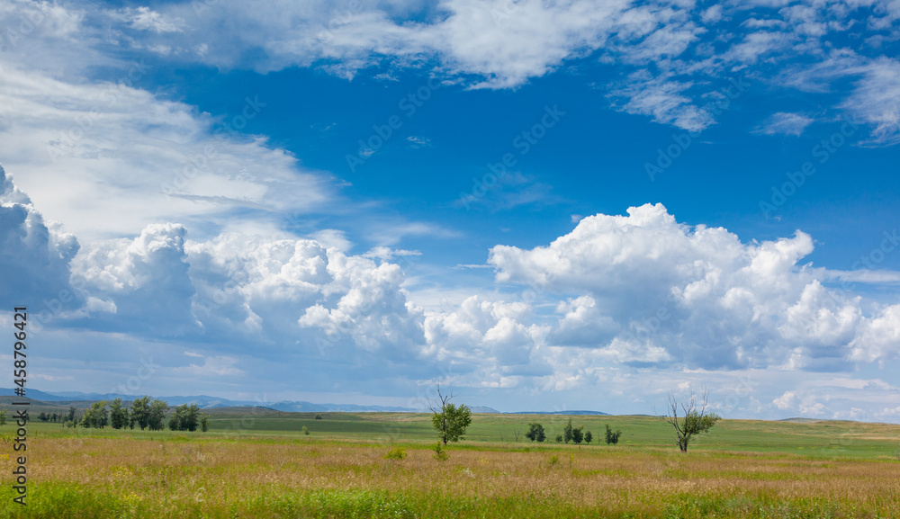 Steppe landscape. Picturesque clouds illuminated by the sun over grass, trees and mountains. Steppe of Khakassia, Russia