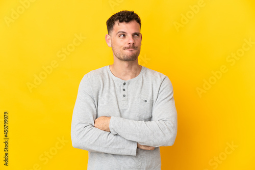 Young caucasian handsome man isolated on yellow background having doubts while looking up