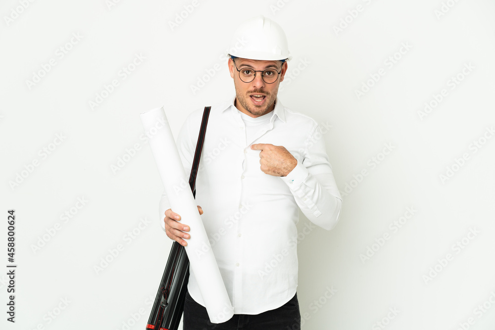 Young architect man with helmet and holding blueprints isolated on white background with surprise facial expression Young architect man with helmet and holding blueprints isolated on white background with surprise facial expression