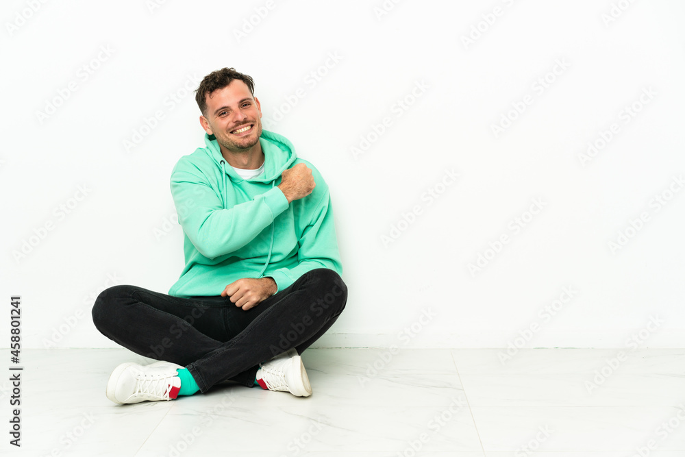 Young handsome caucasian man sitting on the floor celebrating a victory Young handsome caucasian man sitting on the floor celebrating a victory
