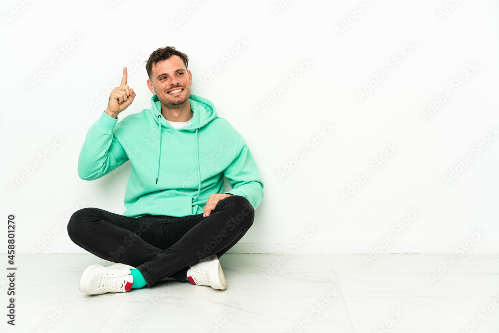 Fototapeta premium Young handsome caucasian man sitting on the floor intending to realizes the solution while lifting a finger up