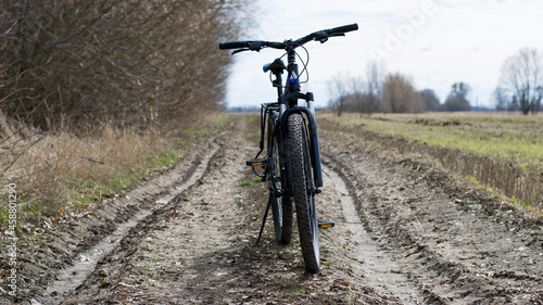Mountain bike. stands on a field road. spring or autumn. concept of cycling, repair or breakage. sports, outdoor activities. bad weather, mud, road washed out after rain. trail, front wheel in focus.