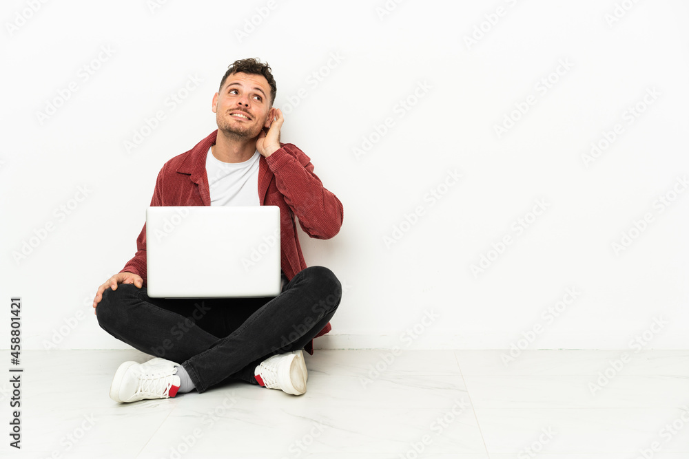 Young handsome caucasian man sit-in on the floor with laptop thinking an idea Young handsome caucasian man sit-in on the floor with laptop thinking an idea