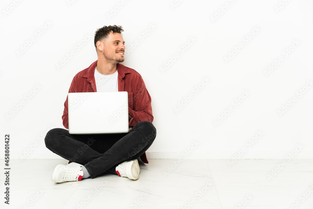Young handsome caucasian man sit-in on the floor with laptop looking side Young handsome caucasian man sit-in on the floor with laptop looking side