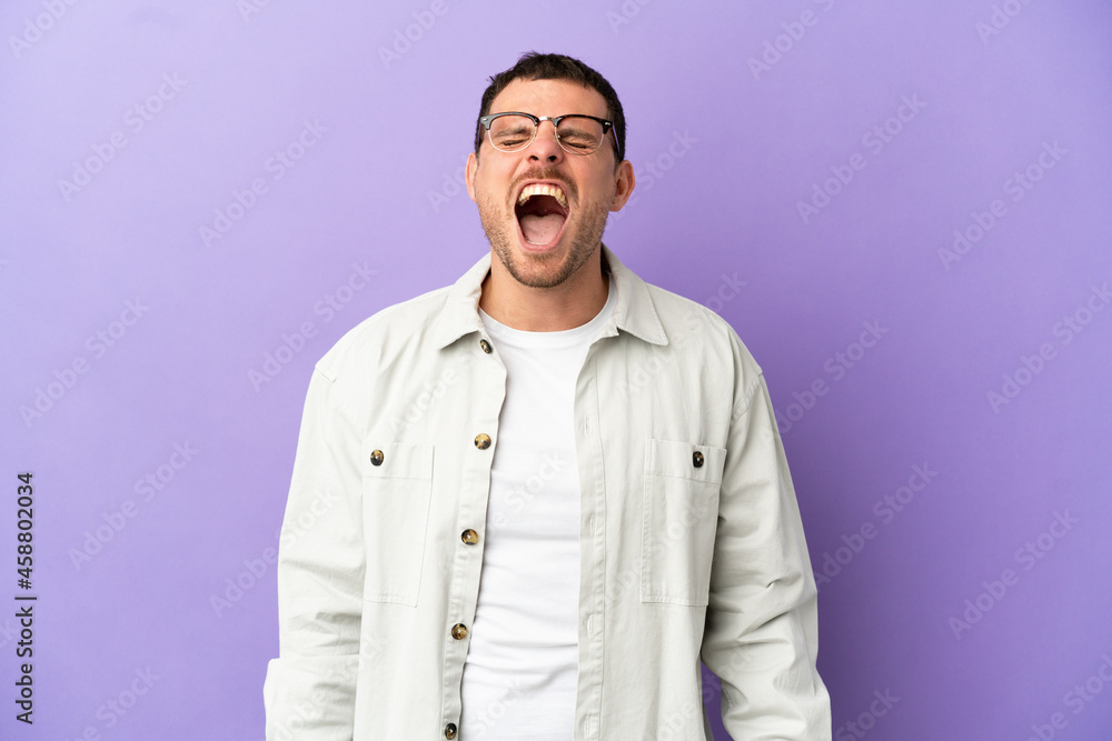 Brazilian man over isolated purple background shouting to the front with mouth wide open Brazilian man over isolated purple background shouting to the front with mouth wide open