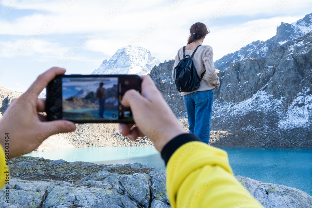 couple hiking on mountain on autumn day. man taking photo on phone of his girlfriend