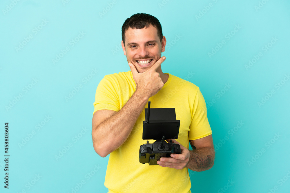 Brazilian man holding a drone remote control over isolated blue background happy and smiling Brazilian man holding a drone remote control over isolated blue background happy and smiling