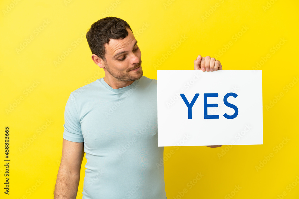 Brazilian man over isolated purple background holding a placard with text YES Brazilian man over isolated purple background holding a placard with text YES