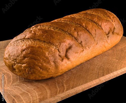 Whole loaf of bread on a wooden board, on a black background