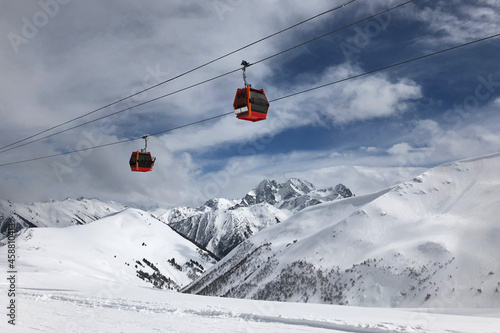 Two red gondolas on sky and cloudly background lift people in high mountains. Active winter leasure concept.