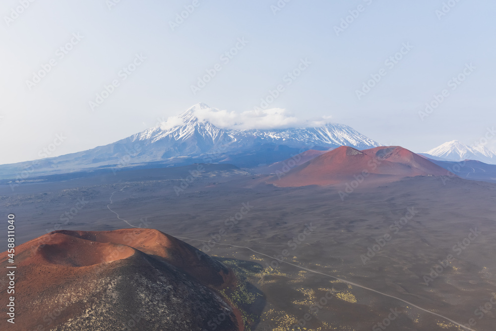 Kamchatka rocks from volcanic rocks multi-colored volcanic rocks. Crumbling volcano craters. against the backdrop of volcanoes with peaks in the snow and clouds. Ostry Tolbachik and Plosky Tolbachik. - obrazy, fototapety, plakaty 