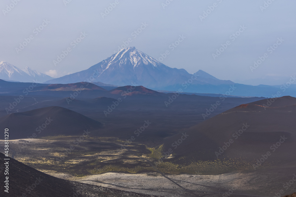 Kamchatka rocks from volcanic rocks multi-colored volcanic rocks. Crumbling volcano craters. against the backdrop of volcanoes with peaks in the snow and clouds. Ostry Tolbachik and Plosky Tolbachik. - obrazy, fototapety, plakaty 