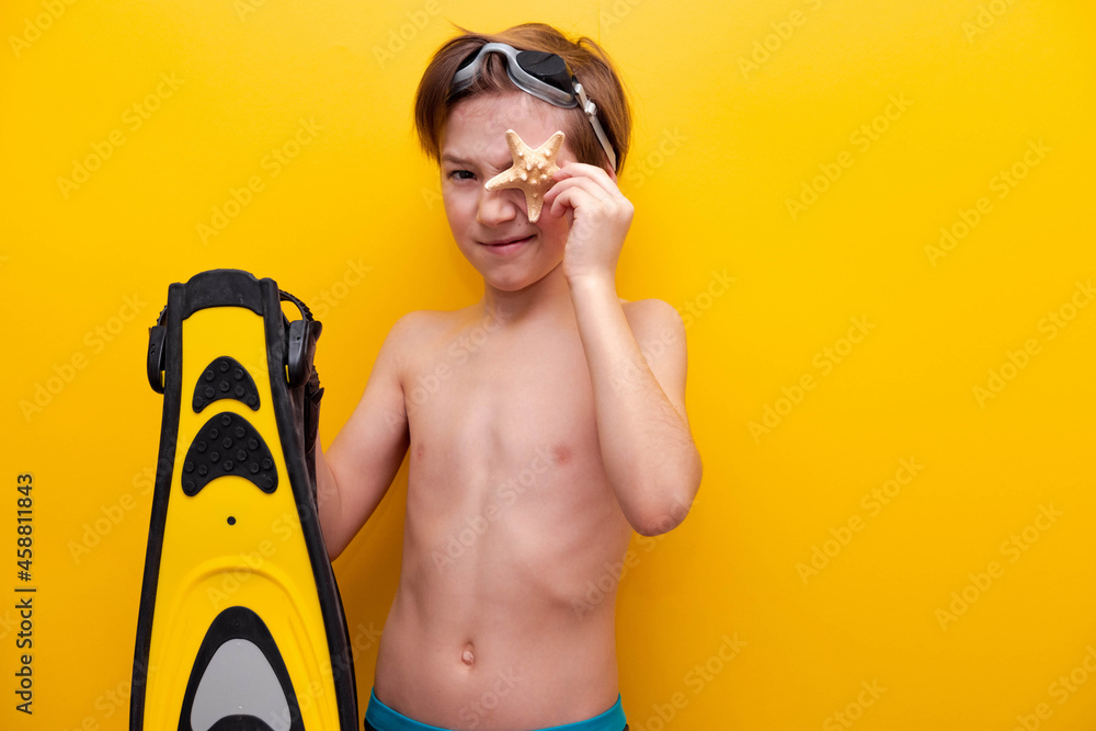 Close-up boy with flippers and starfish with yellow background. Traveling on vacation at sea with children. Summer vacation at school basis for banner - obrazy, fototapety, plakaty 