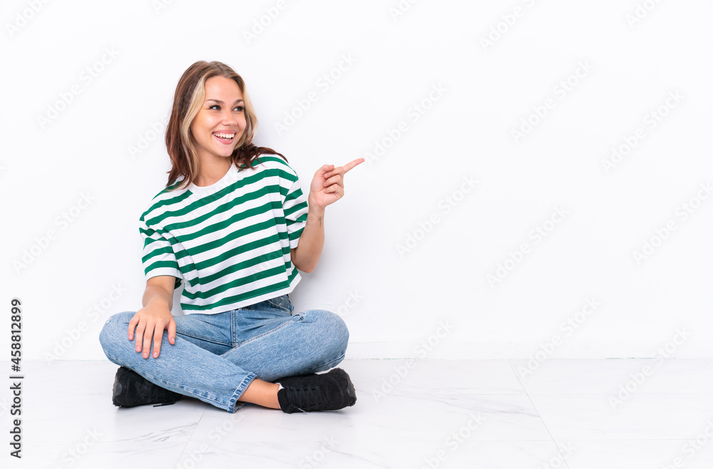 Young Russian girl sitting on the floor isolated on white background pointing finger to the side and presenting a product Young Russian girl sitting on the floor isolated on white background pointing finger to the side and presenting a product