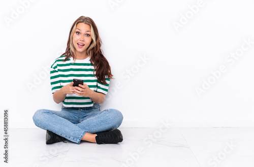 Young Russian girl sitting on the floor isolated on white background surprised and sending a message