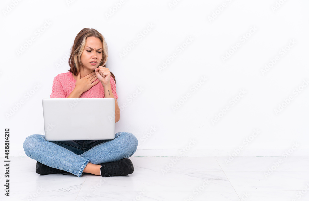 Young Russian girl with a laptop sitting on the floor isolated on white background is suffering with cough and feeling bad Young Russian girl with a laptop sitting on the floor isolated on white background is suffering with cough and feeling bad