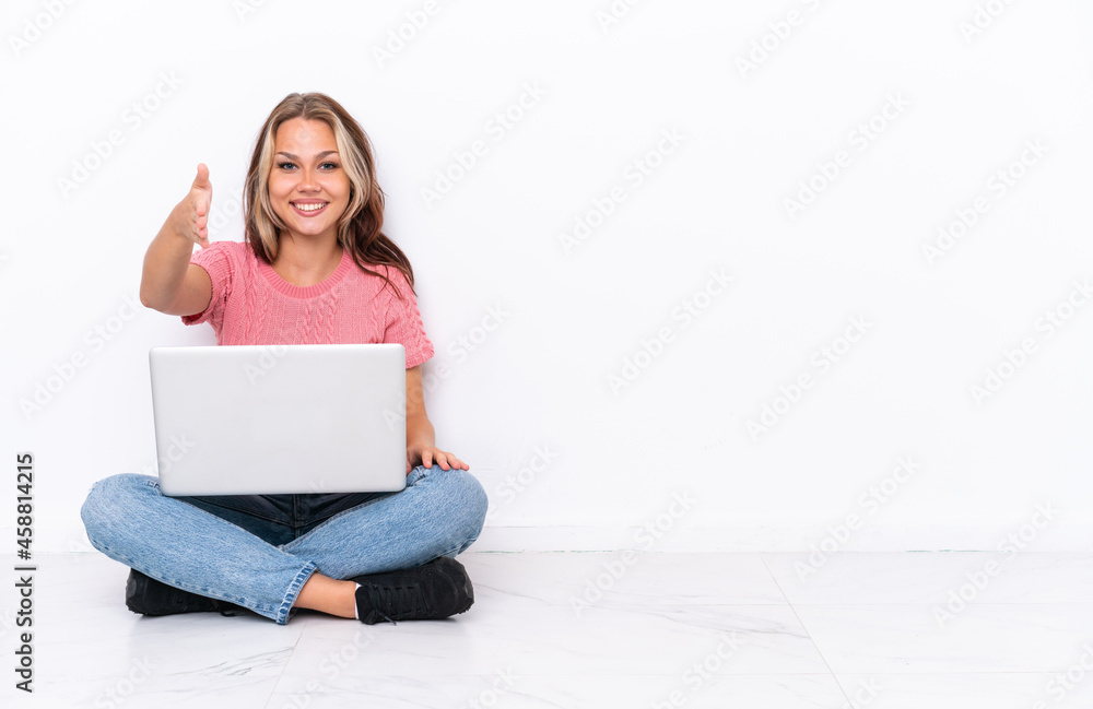 Young Russian girl with a laptop sitting on the floor isolated on white background shaking hands for closing a good deal Young Russian girl with a laptop sitting on the floor isolated on white background shaking hands for closing a good deal