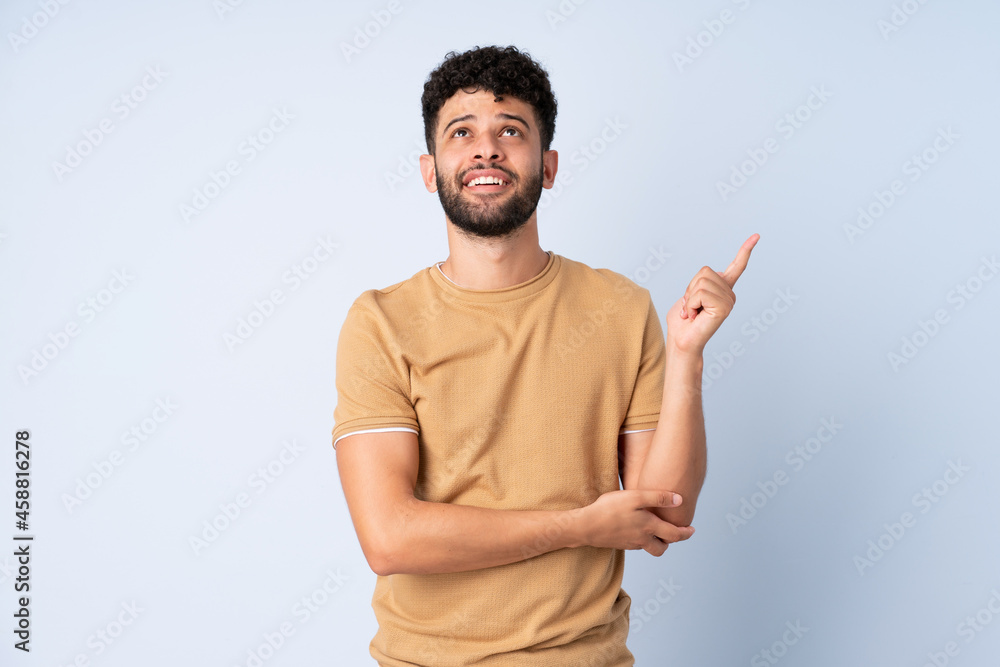 Young Moroccan man isolated on blue background pointing up a great idea Young Moroccan man isolated on blue background pointing up a great idea