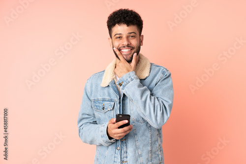 Young Moroccan man using mobile phone isolated on pink background happy and smiling © luismolinero
