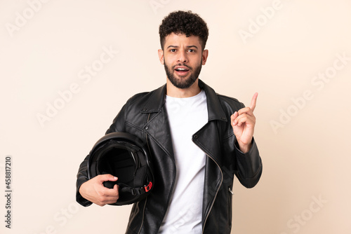 Young Moroccan man with a motorcycle helmet isolated on beige background intending to realizes the solution while lifting a finger up © luismolinero