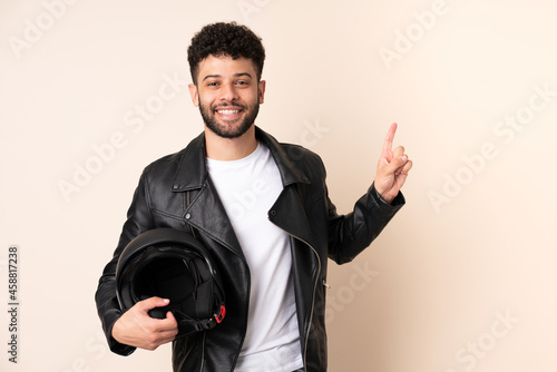 Young Moroccan man with a motorcycle helmet isolated on beige background showing and lifting a finger in sign of the best © luismolinero