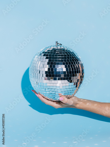 Shiny disco ball in a woman s hand isolated on a bright blue background. Ball part effect  nightlife  and celebration inspired idea. Creative New Year party or festive concept. Fashion minimal art.