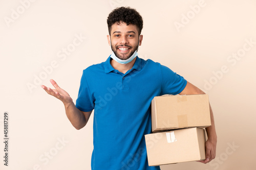 Young delivery Moroccan man isolated on beige background with shocked facial expression