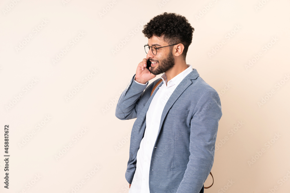 Young business Moroccan man isolated on beige background keeping a conversation with the mobile phone with someone
