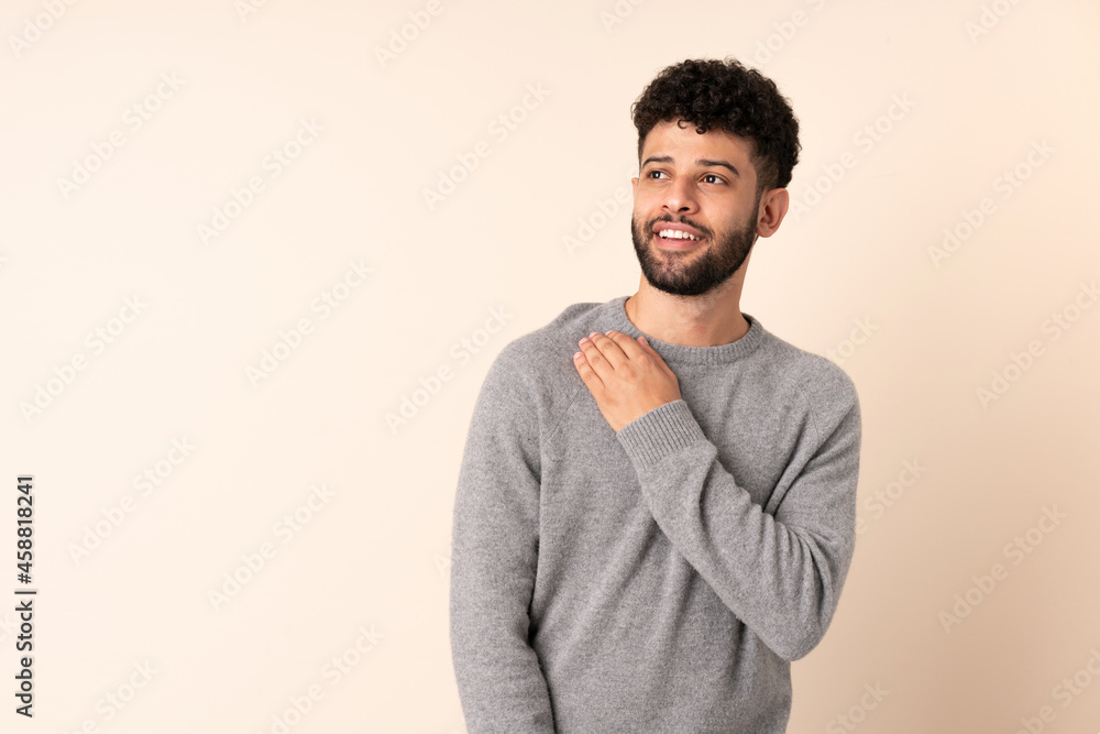 Young Moroccan man isolated on beige background looking up while smiling Young Moroccan man isolated on beige background looking up while smiling