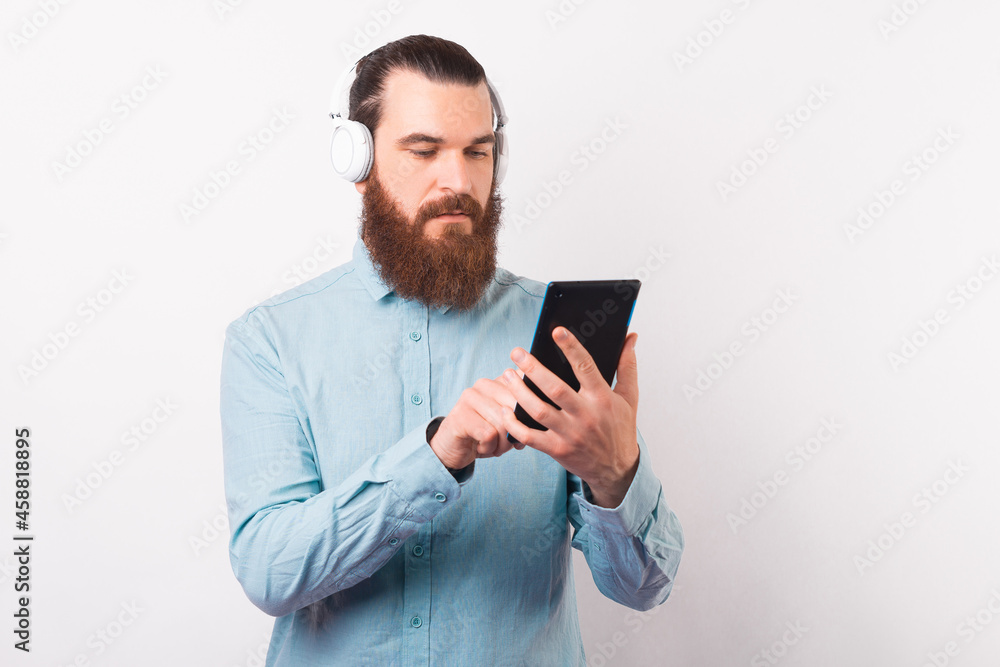Young serious man is using a tablet and wearing some earphones over white background. Young serious man is using a tablet and wearing some earphones over white background.