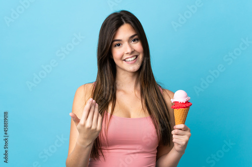 Teenager Brazilian girl holding a cornet ice cream over isolated blue background inviting to come with hand. Happy that you came