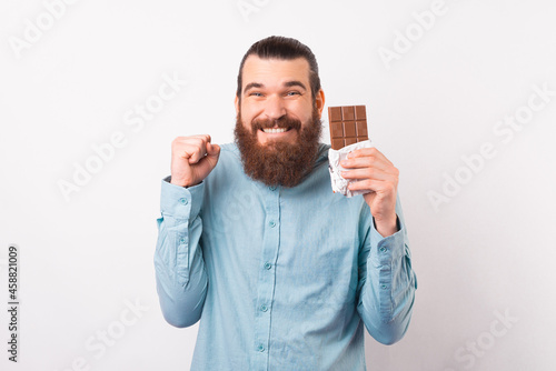 Bearded man is excited about a chocolate break while holding one over white background.