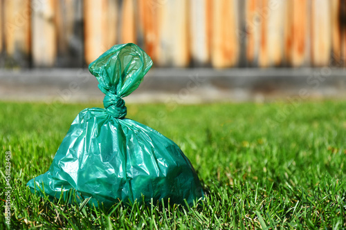 A close up image of a full green plastic dog poop bag on a lush green lawn. 