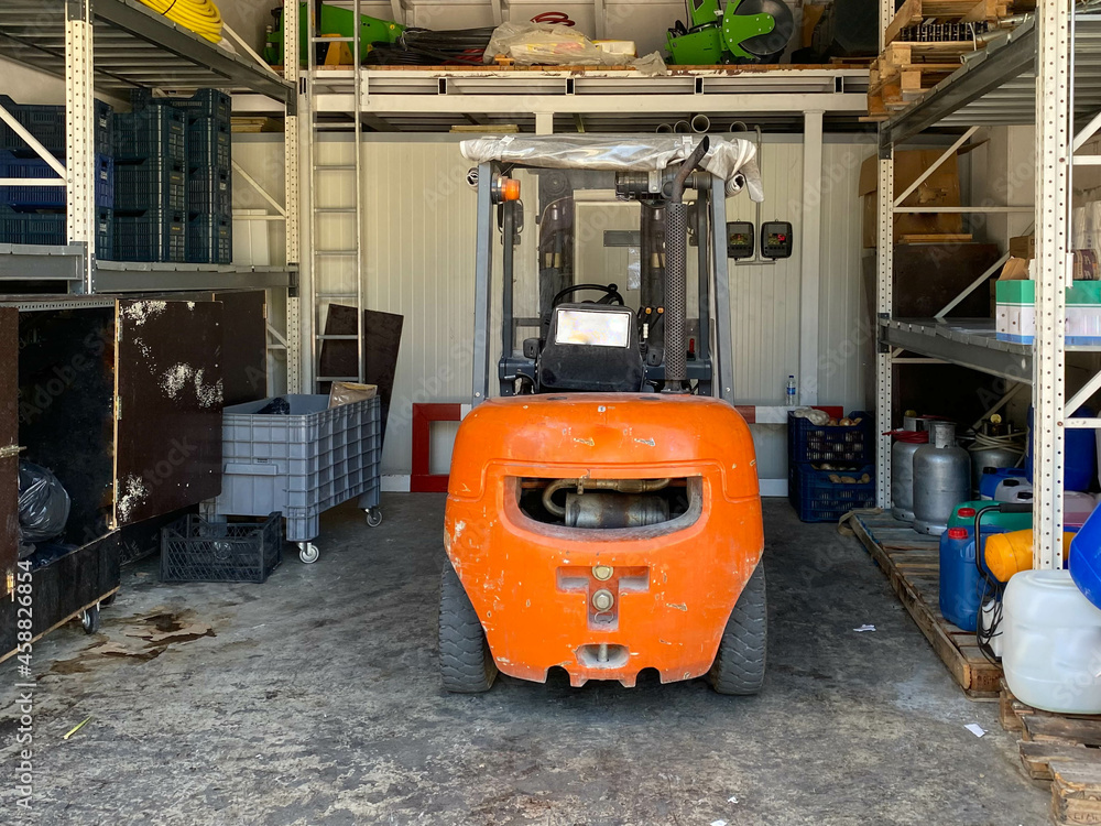 An orange industrial forklift truck stands in a garage for maintenance