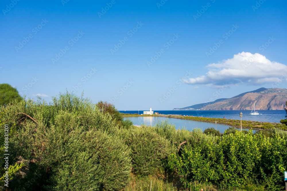 Salina island (Aeolian archipelago), Messina, Sicily, Italy, 08.17.2021: view of the salt lake with the white lighthouse in the background in Punta Lingua. Salina island (Aeolian archipelago), Messina, Sicily, Italy, 08.17.2021: view of the salt lake with the white lighthouse in the background in Punta Lingua.