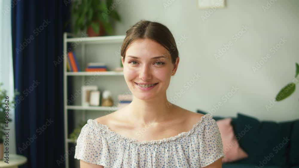 Happy woman portrait. Young mother sitting on sofa in living room, smiling and looking in camera. Female person model posing on couch with cute smile at home. 