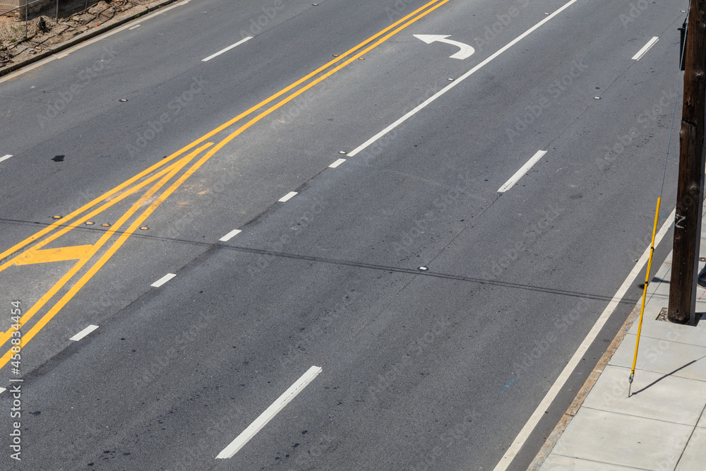 Overhead view of an urban street with four lanes plus a turn lane, asphalt and concrete, horizontal aspect