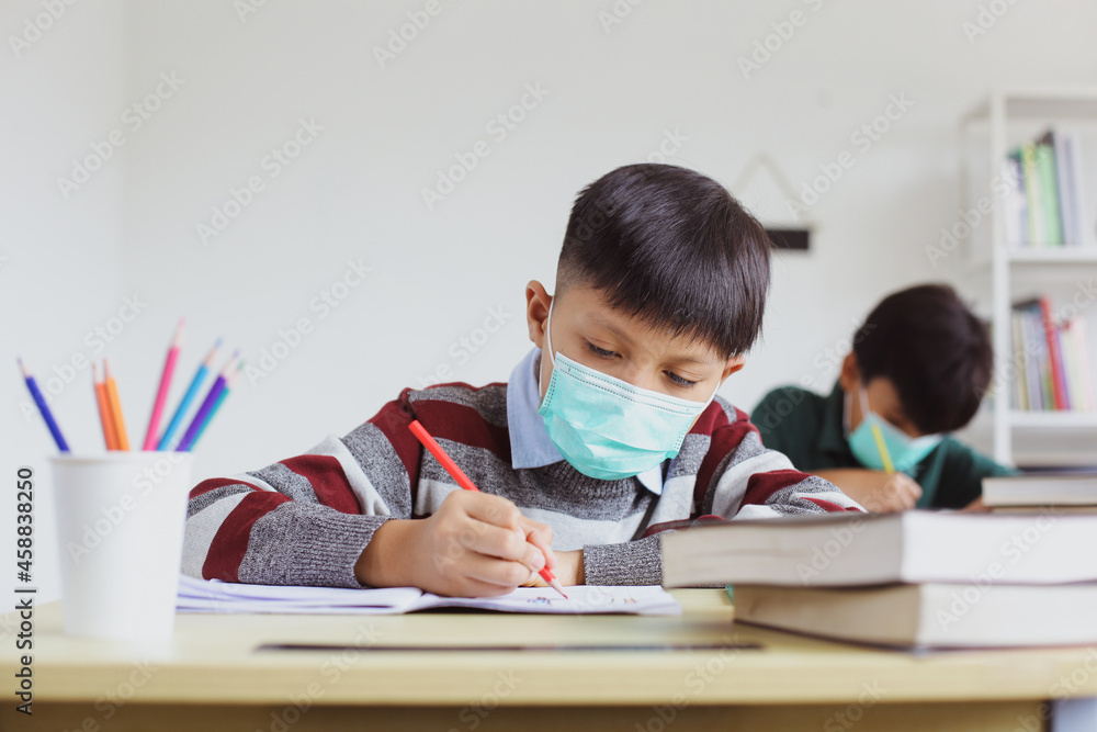 Asian schoolboy in medical mask are writing on a book and doing assignments in class Asian schoolboy in medical mask are writing on a book and doing assignments in class