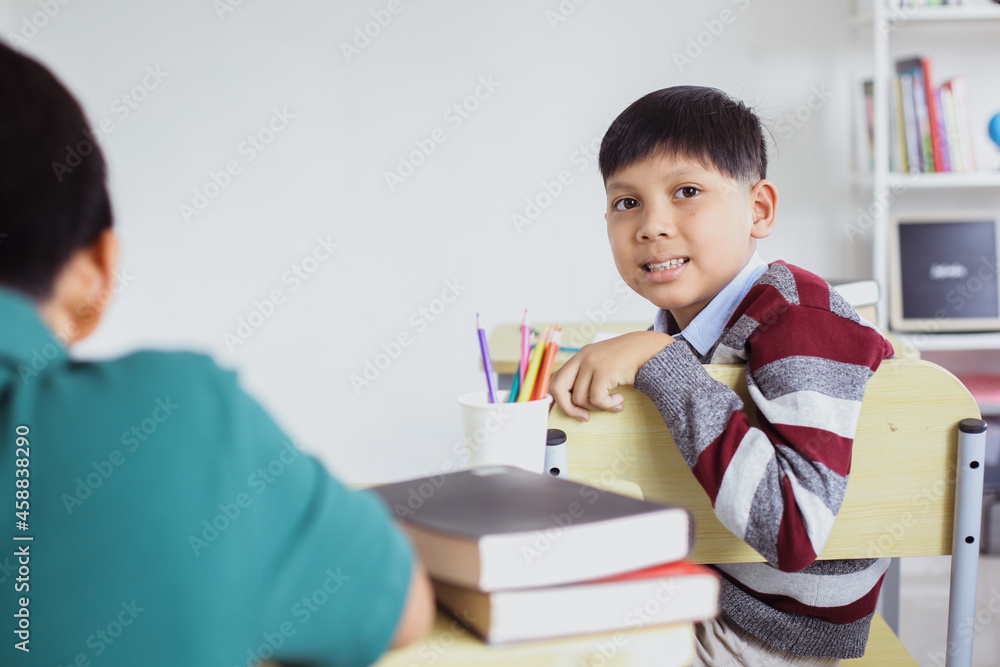 Smiling Asian student sitting on the chair while looking to the camera in a classroom Smiling Asian student sitting on the chair while looking to the camera in a classroom