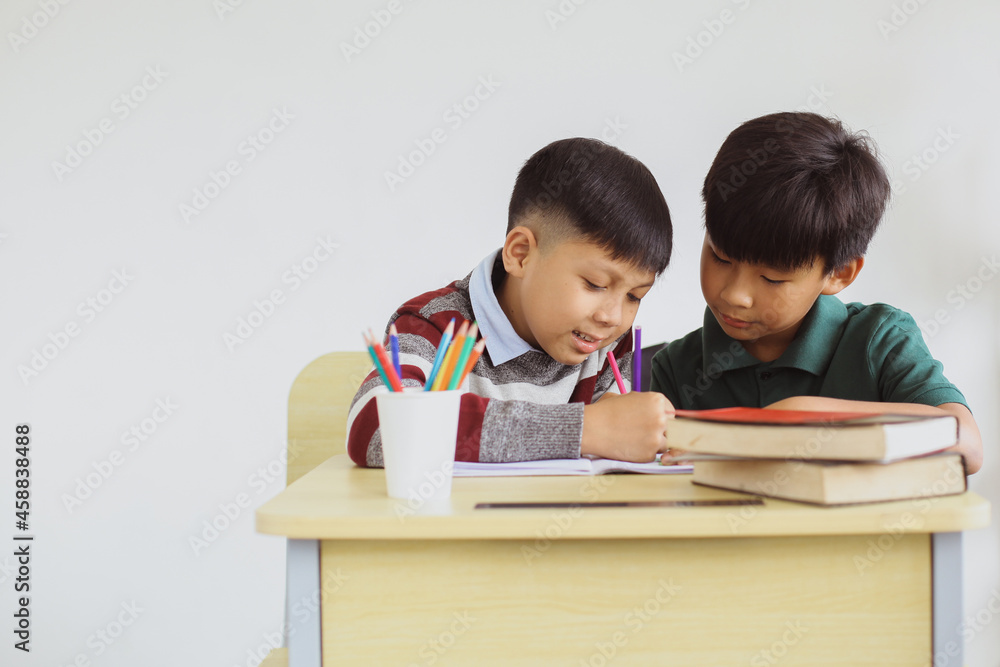 Two Asian students studying and writing together on a book in a classroom Two Asian students studying and writing together on a book in a classroom