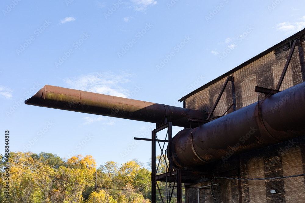 Giant pipe tubes wrapping and emanating from an old industrial warehouse building, fall season landscape and blue skies, horizontal aspect