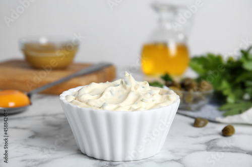 Tasty tartar sauce and ingredients on white marble table